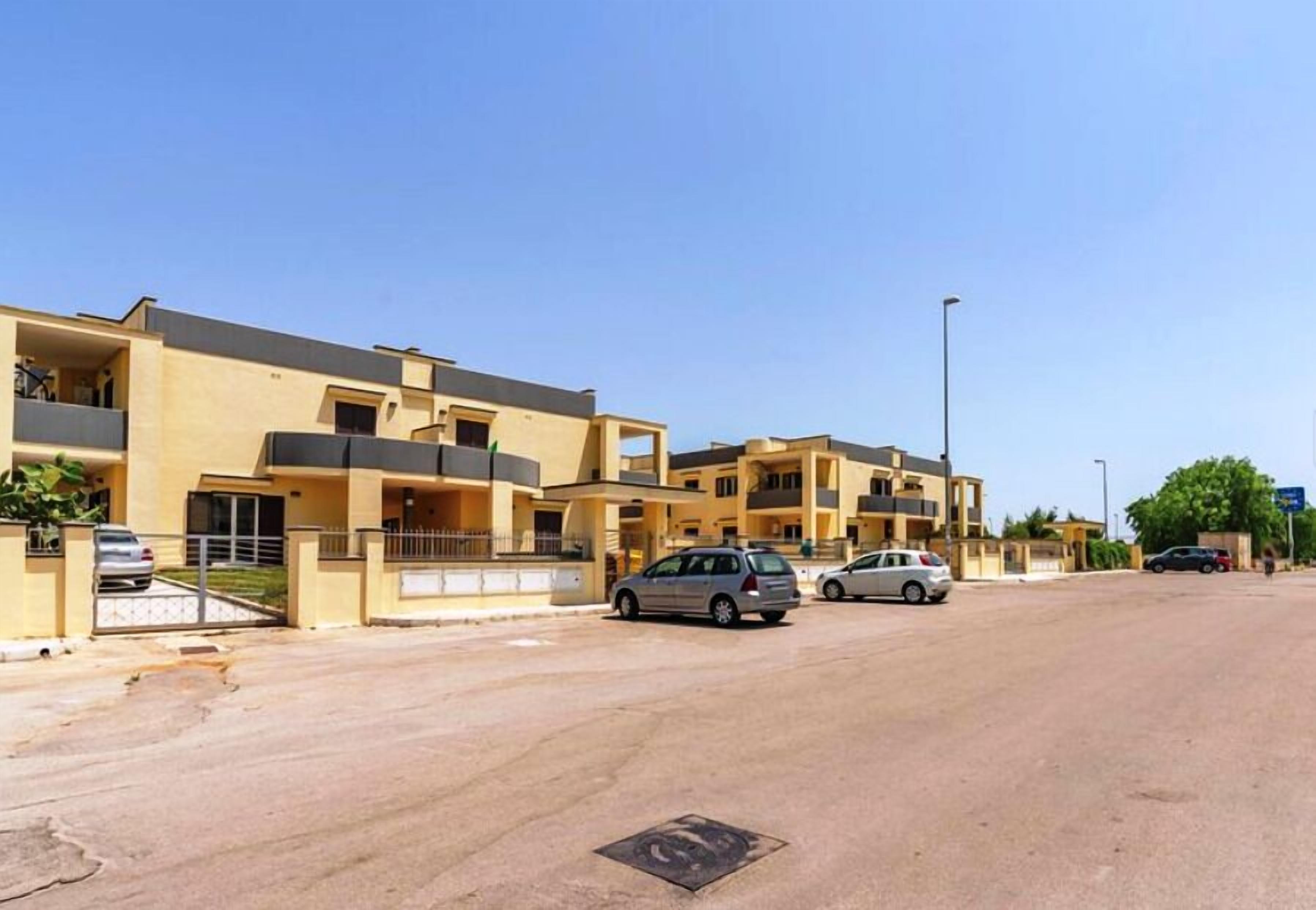 A residential area with multi-story buildings, a paved road, and parked cars.