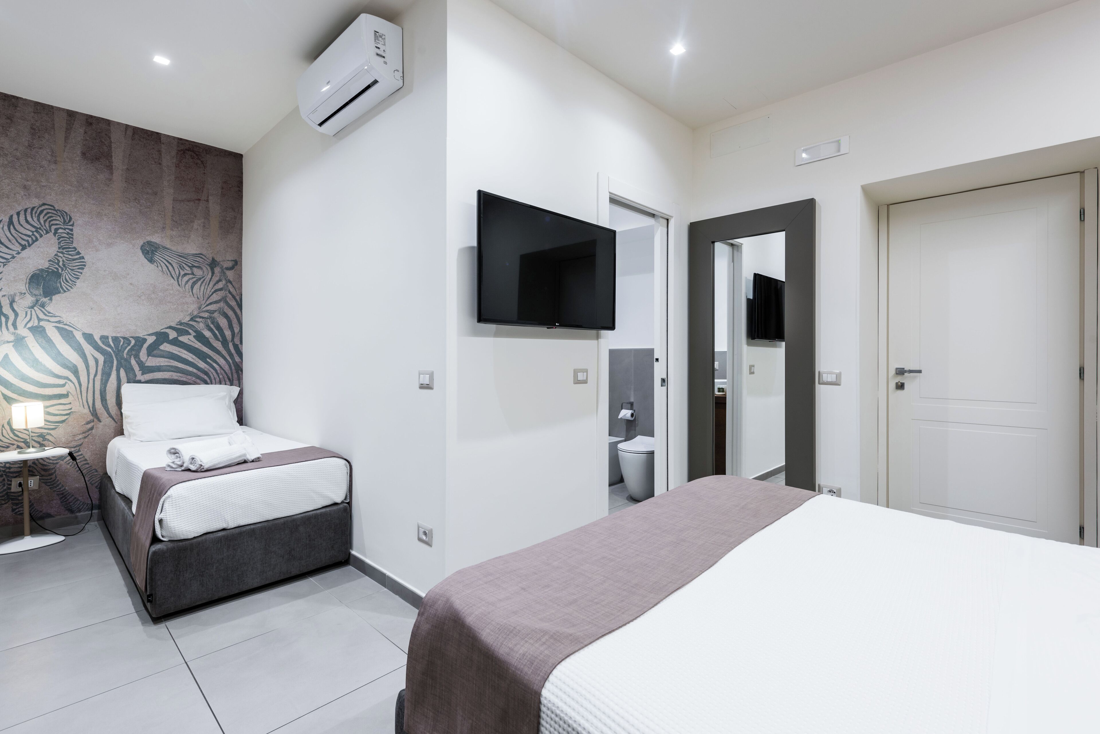 Una habitación de hotel moderna con una cama grande, un televisor de pantalla plana, aire acondicionado en la pared y un mural con cebras.