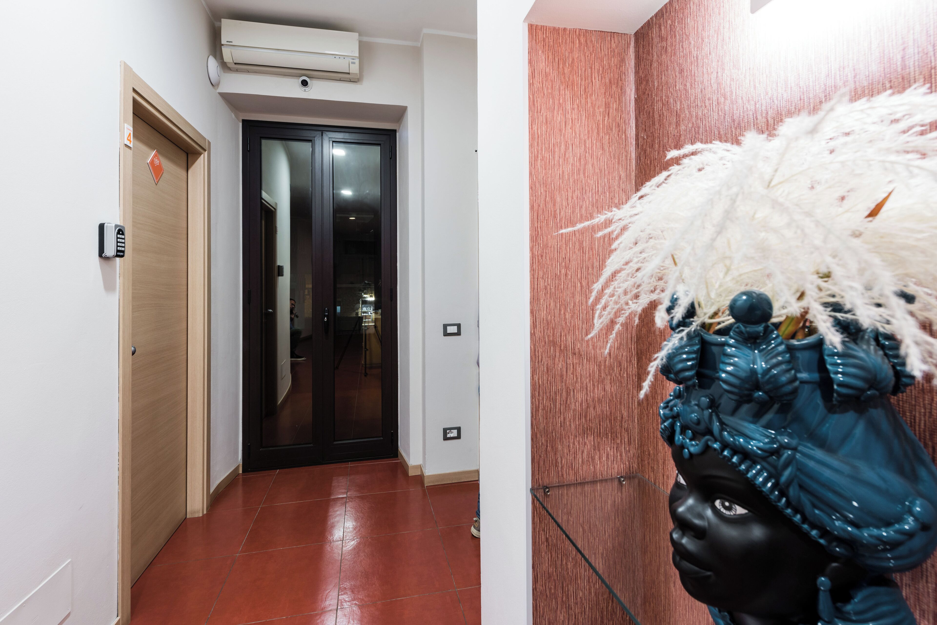 Un pasillo con una puerta de madera, una puerta con marco negro y un aire acondicionado instalado en la pared.