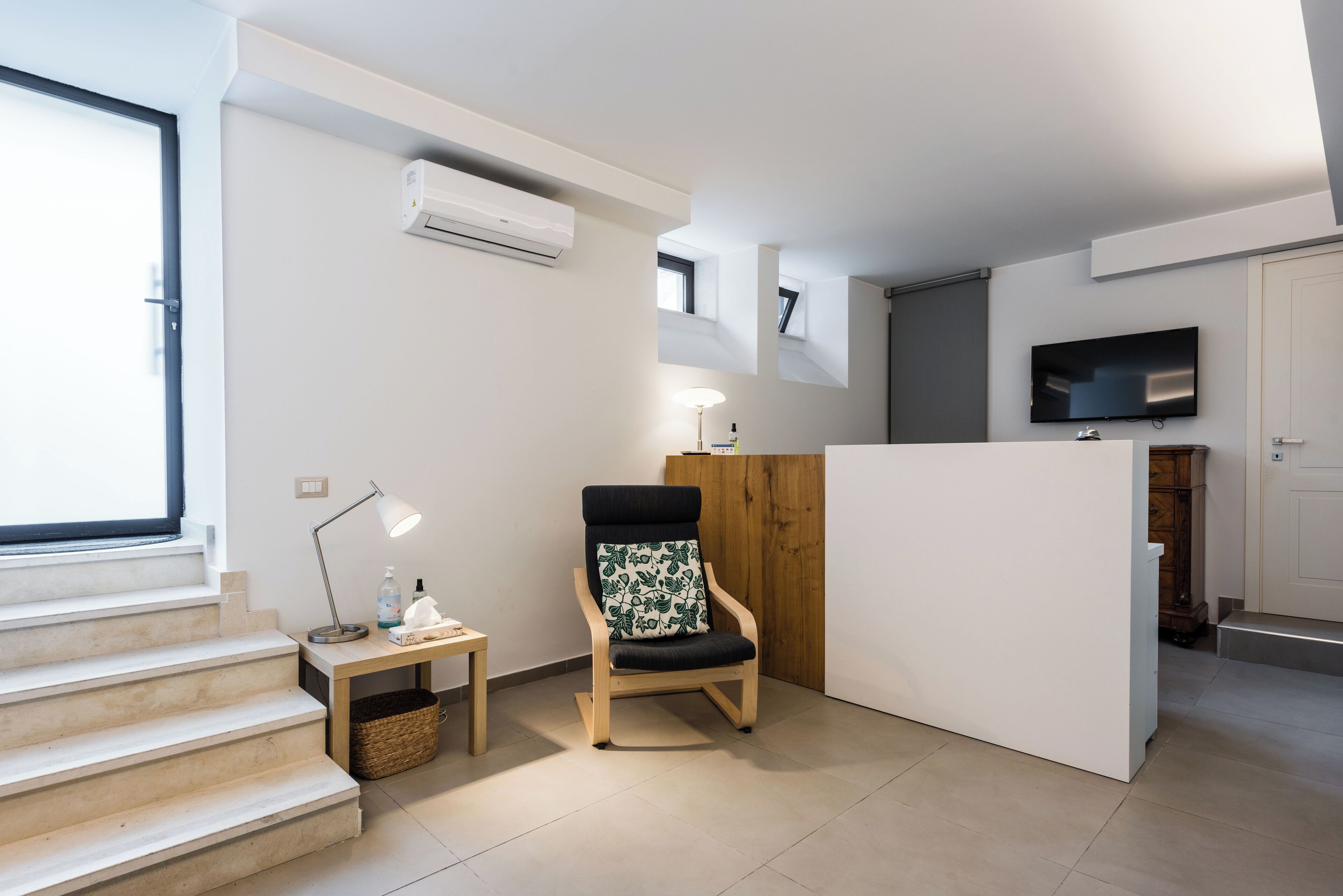 Un appartamento moderno con una sedia in legno, un tavolino con una lampada, una TV e una scala.