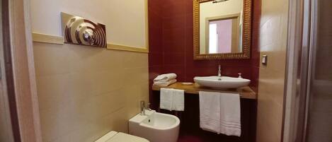 A compact bathroom with a toilet, sink, and bidet. A towel rack holds two towels.