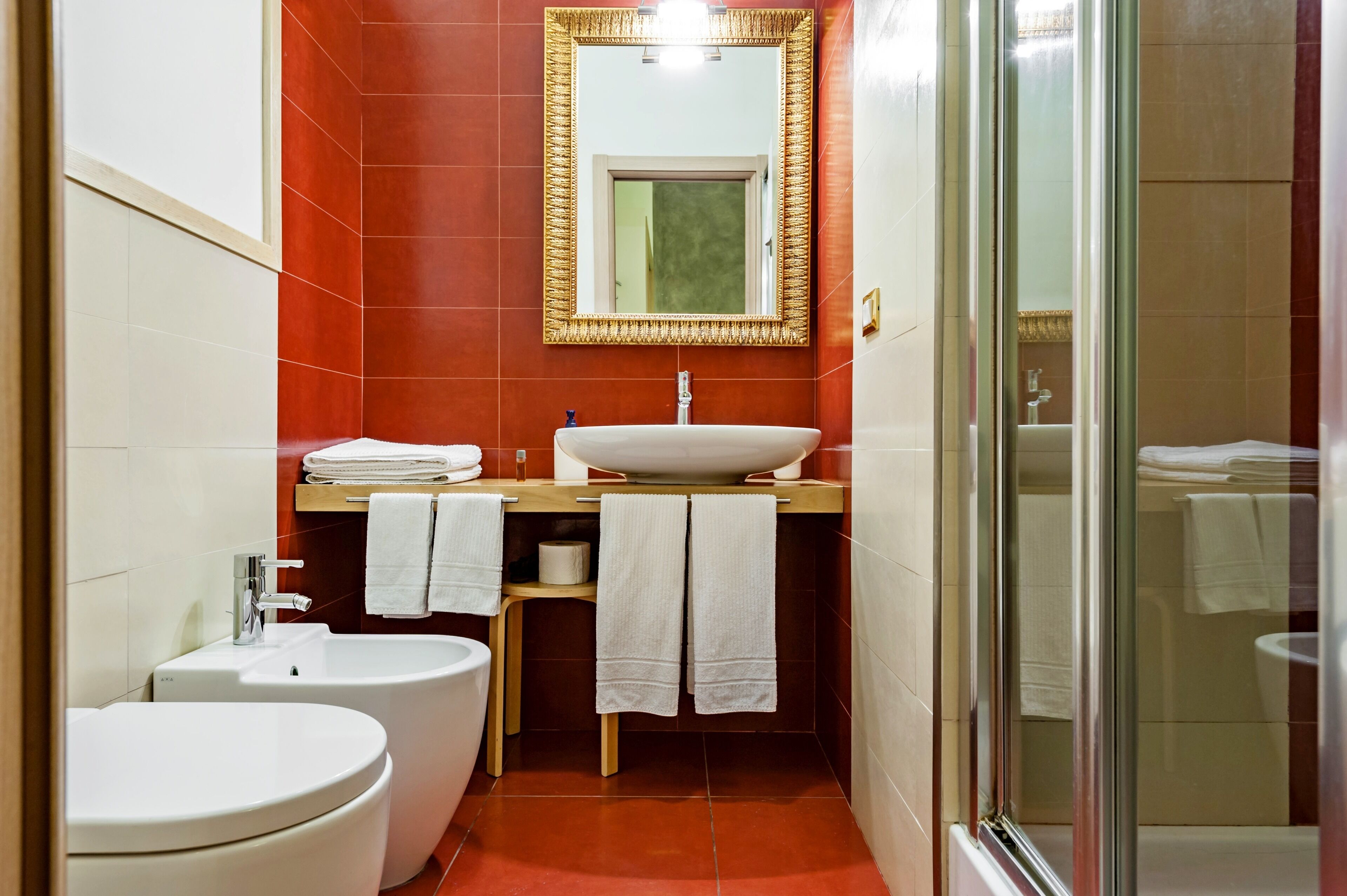 Un baño con lavamanos blanco, inodoro y bidé. Hay un espejo sobre el lavamanos y una puerta de ducha de vidrio.
