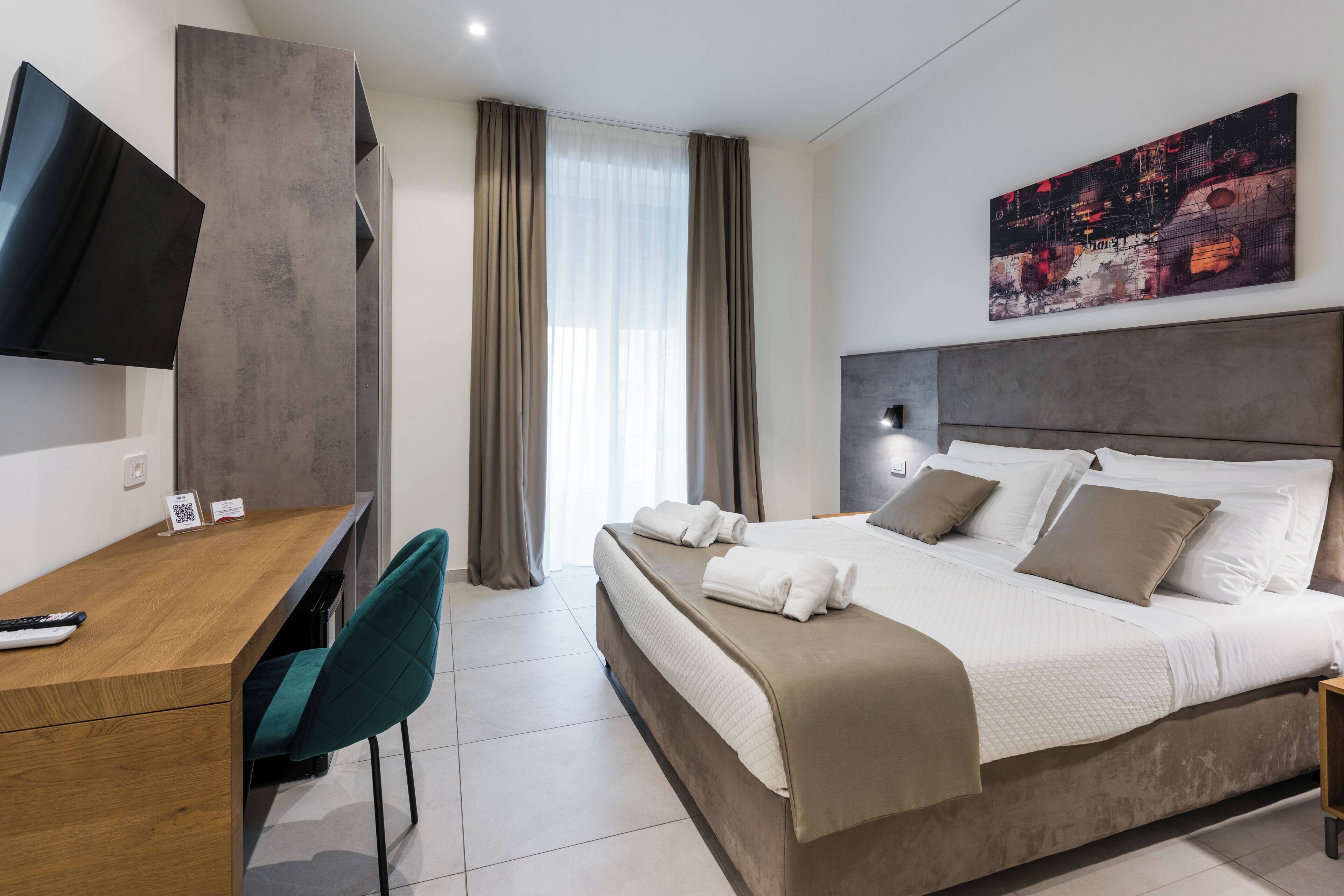 Una habitación de hotel moderna con una cama, un escritorio, una silla, un televisor y un cuadro en la pared.