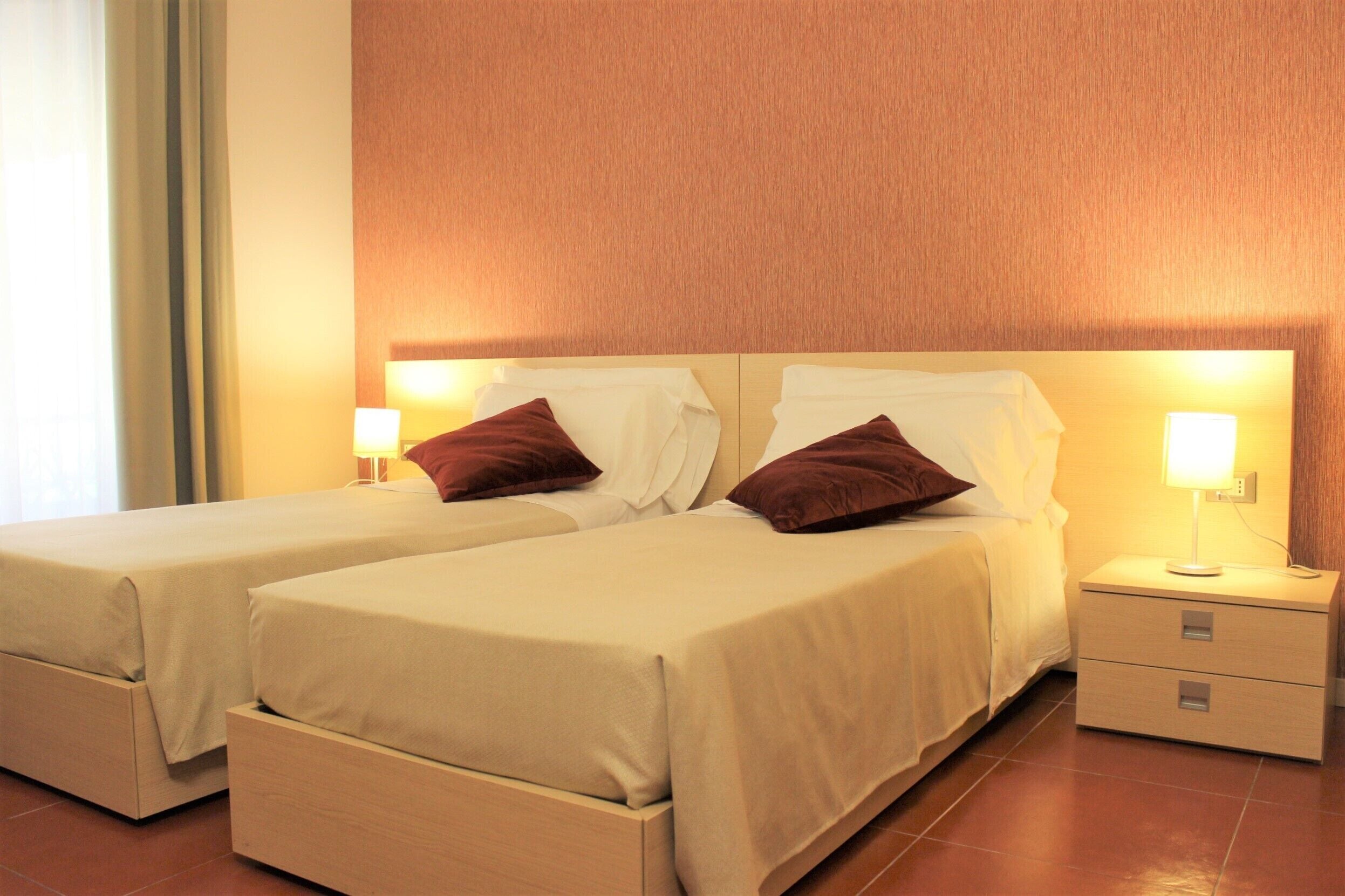 Ein Doppelzimmer mit zwei Betten, jeweils mit Kissen und einem Nachttisch mit Lampe.