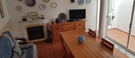 Ein Wohnzimmer mit Kamin, einem Fernseher auf einem Holzschrank, einem Esstisch mit Stühlen und verschiedenen dekorativen Tellern an der Wand.