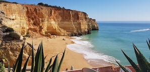 A coastal beach with a cliff, clear blue sea, and a few people. - Beach house in Benagil, praia do Carvoeiro (Carvoeiro)