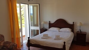 Een slaapkamer met een bed, twee nachtkastjes, een stoel en een glazen schuifdeur naar een buitenruimte.