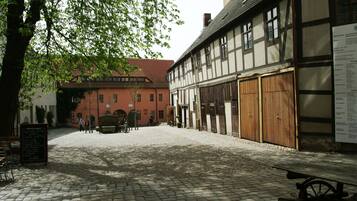 A cobblestone courtyard with a traditional half-timbered building, a red brick building, and a signboard.