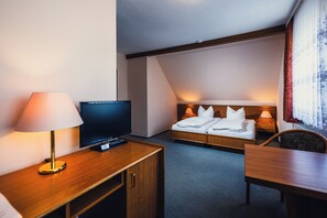 Ein Hotelzimmer mit einem Bett, einem Schreibtisch mit Lampe, einem Fernseher und einem Fenster mit Vorhängen.
