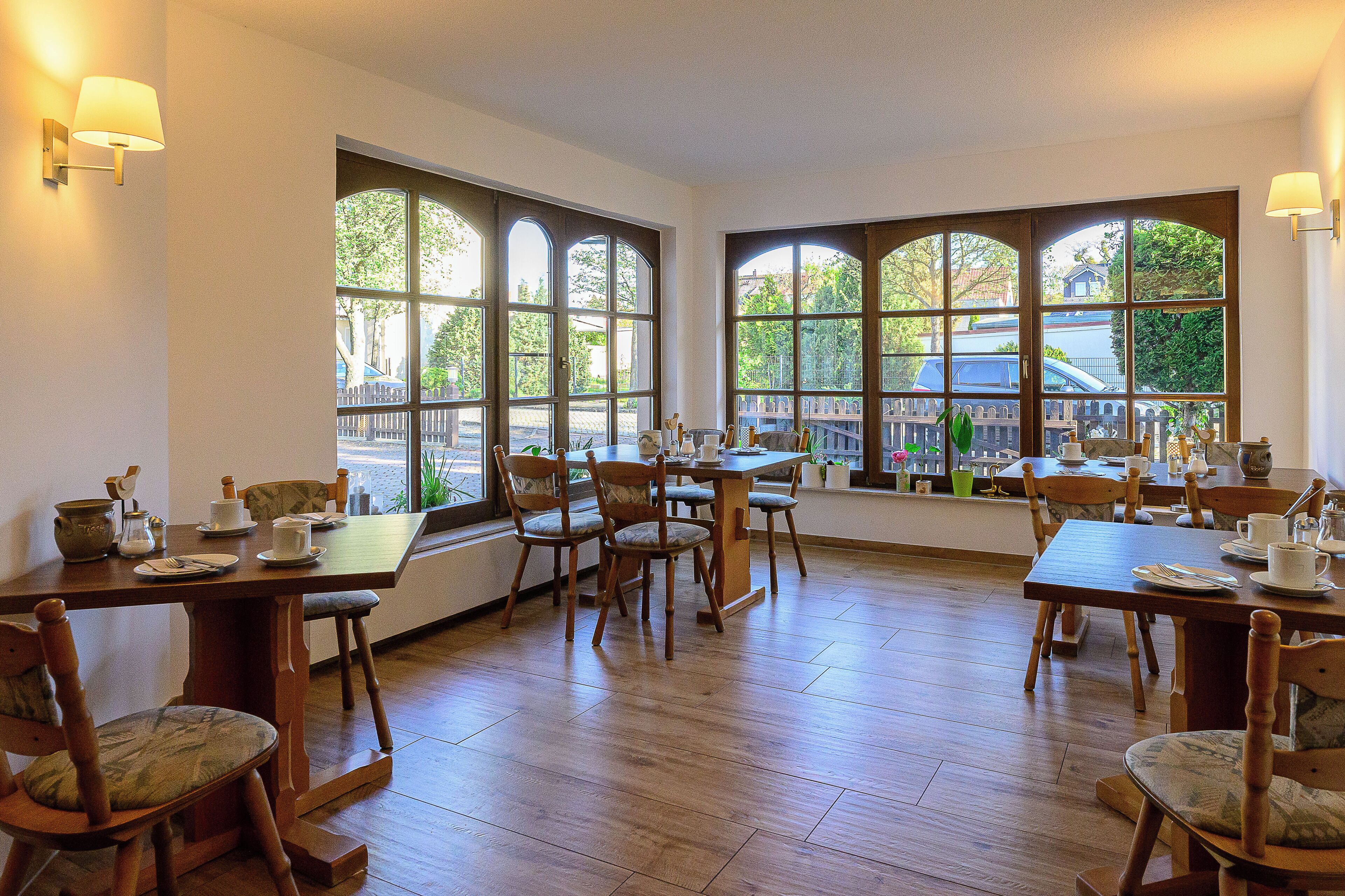 A dining area with wooden tables and chairs, large windows with arched tops, and a view of the outdoors.