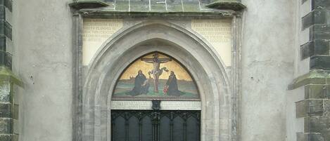 Entrada de uma igreja com um grande arco, uma janela de vitrais acima e duas estátuas de cada lado.