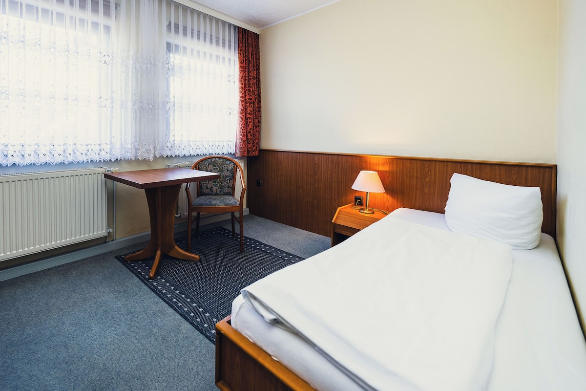 A hotel room with a bed, a desk, a chair, a lamp, and a window with curtains.
