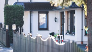 Un bâtiment blanc avec un toit noir, une clôture en bois et une petite fenêtre ornée d’une lanterne suspendue.