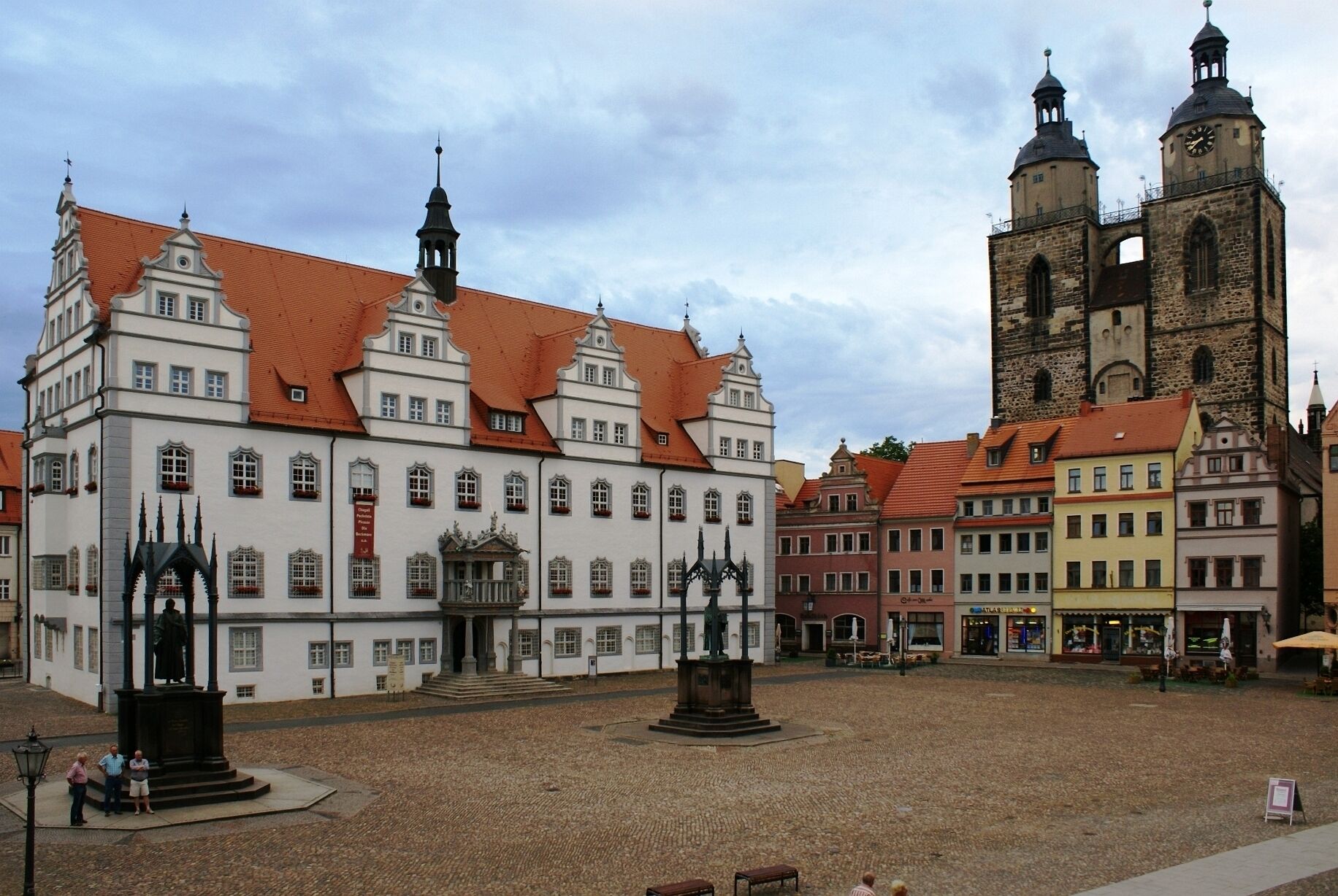 Ein historisches Gebäude mit rotem Ziegeldach, einem markanten Glockenturm und einer Statue im Innenhof.