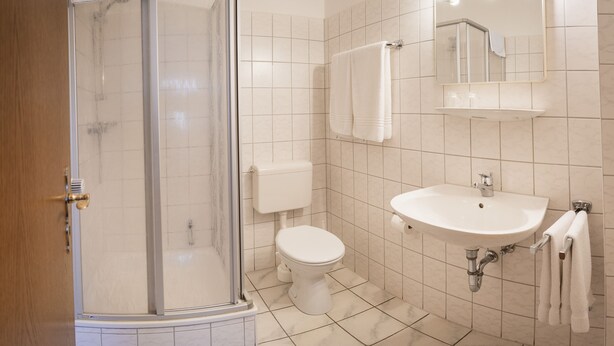 Ein Badezimmer mit Duschkabine, Toilette, Waschbecken und beleuchtetem Spiegel.