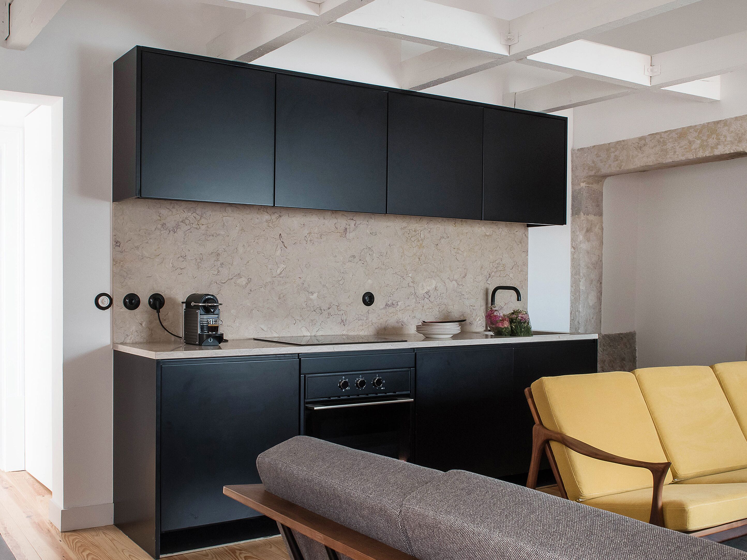 A modern kitchen with dark cabinets, a marble backsplash, and a yellow chair.