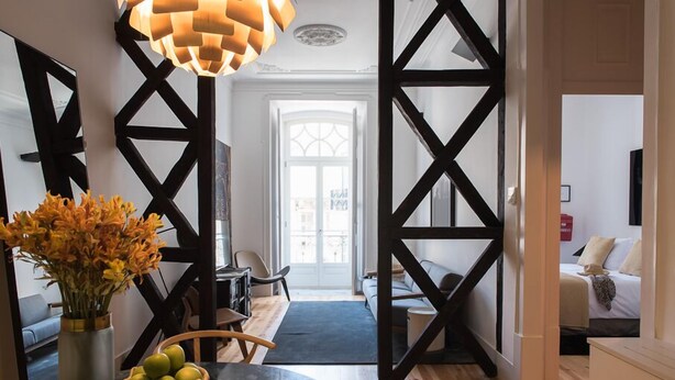 Un salon moderne avec un canapé à cadre noir, une table à manger agrémentée d’un vase de fleurs et une grande fenêtre offrant une vue sur la ville.
