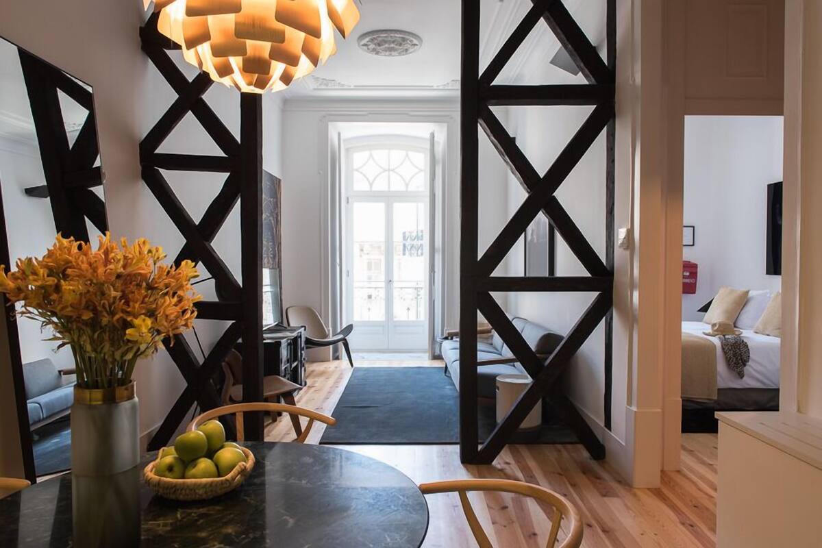 Una sala de estar moderna con un sofá de marco negro, una mesa de comedor con un florero y un ventanal con vistas a la ciudad.