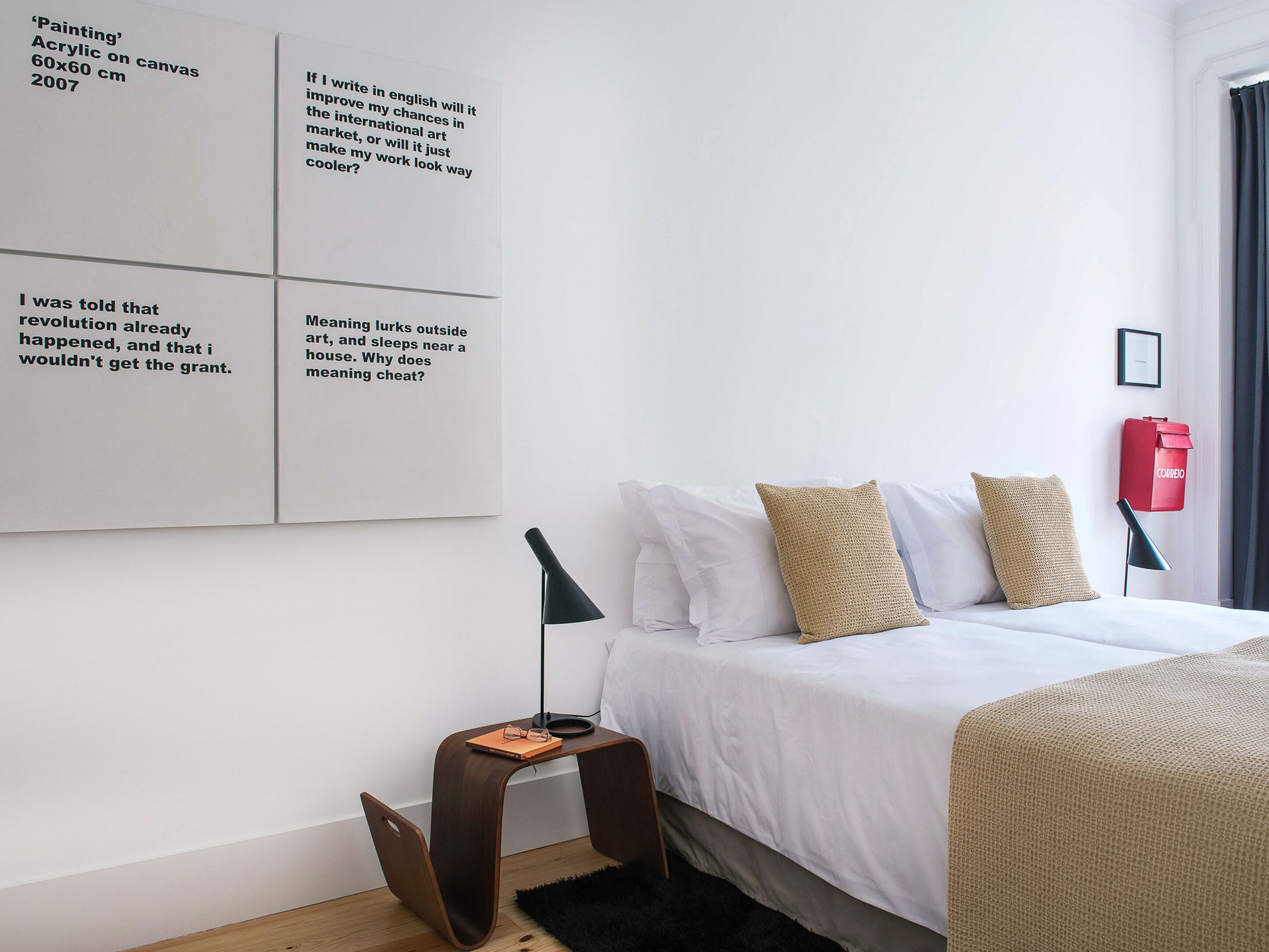 Une chambre d’hôtel moderne avec un lit bien fait, une petite table d’appoint et une œuvre d’art murale comportant du texte.