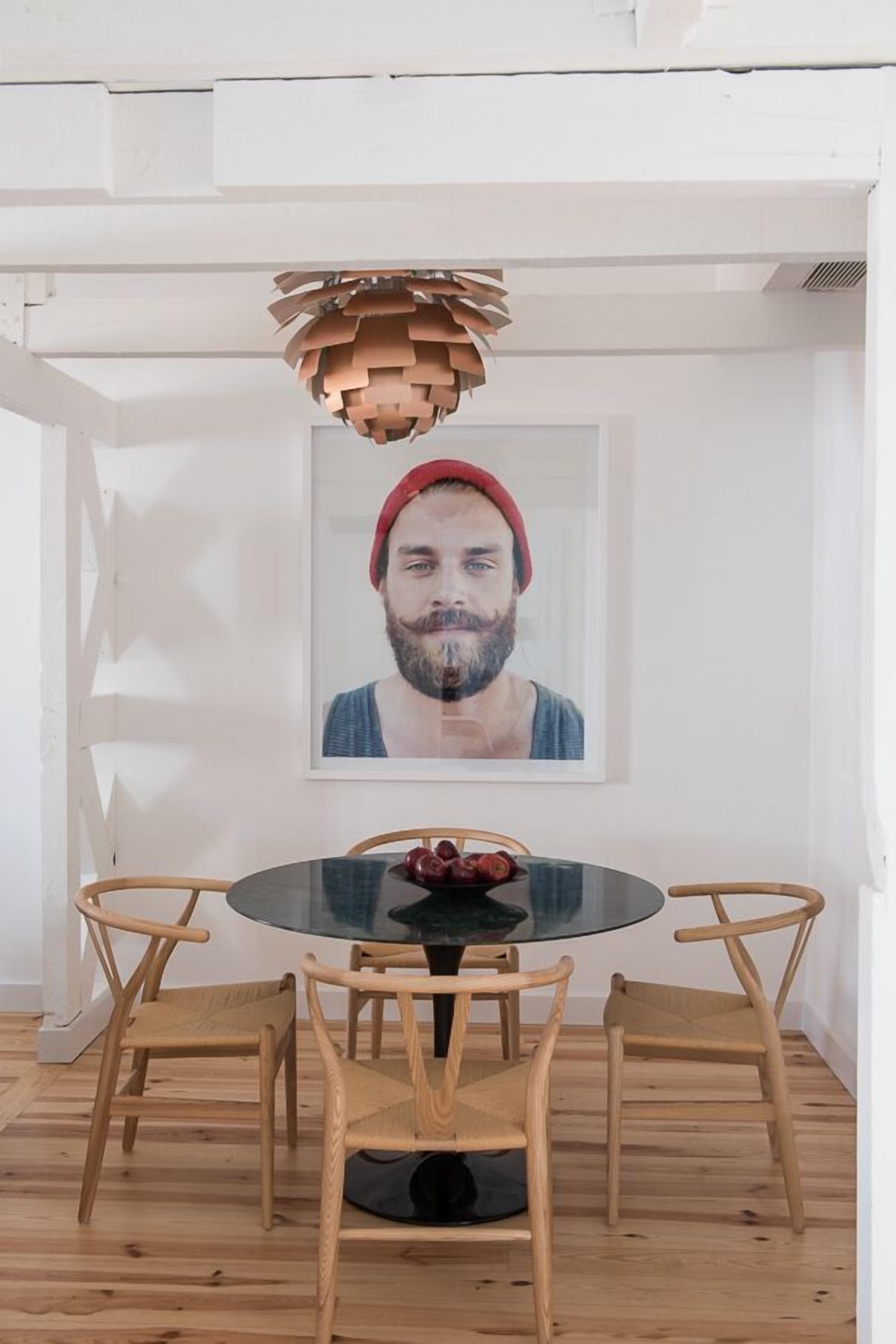 A dining area with a round glass table, wooden chairs, and a unique hanging light fixture.