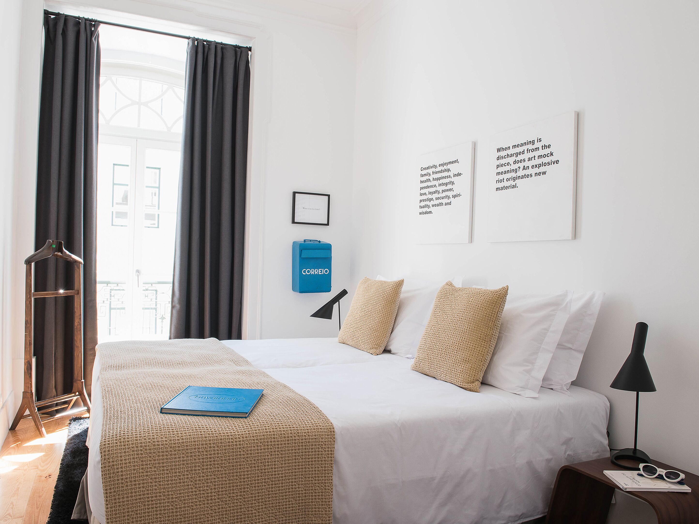 Una camera d'albergo con un letto, un minibar blu, una lampada nera e due cuscini.