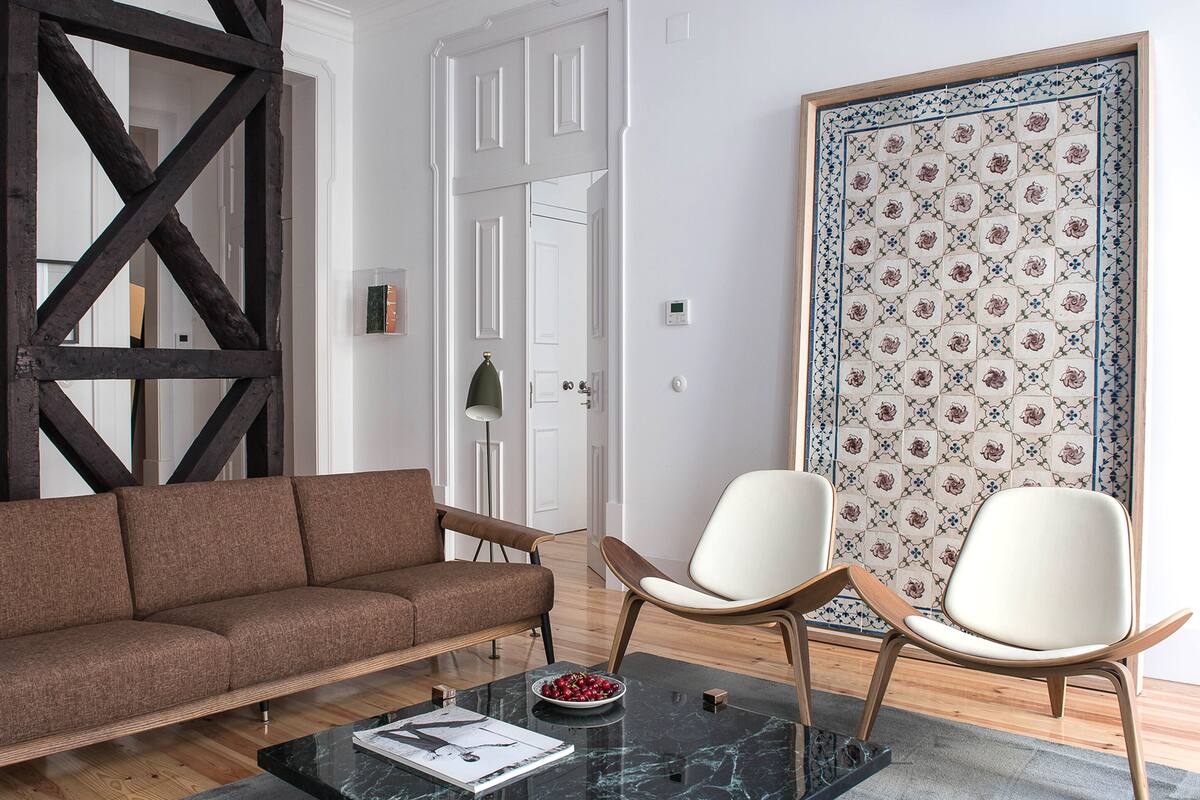 Una sala de estar moderna con un sofá marrón, dos sillas blancas, una mesa de centro de vidrio y una pared con estampado.