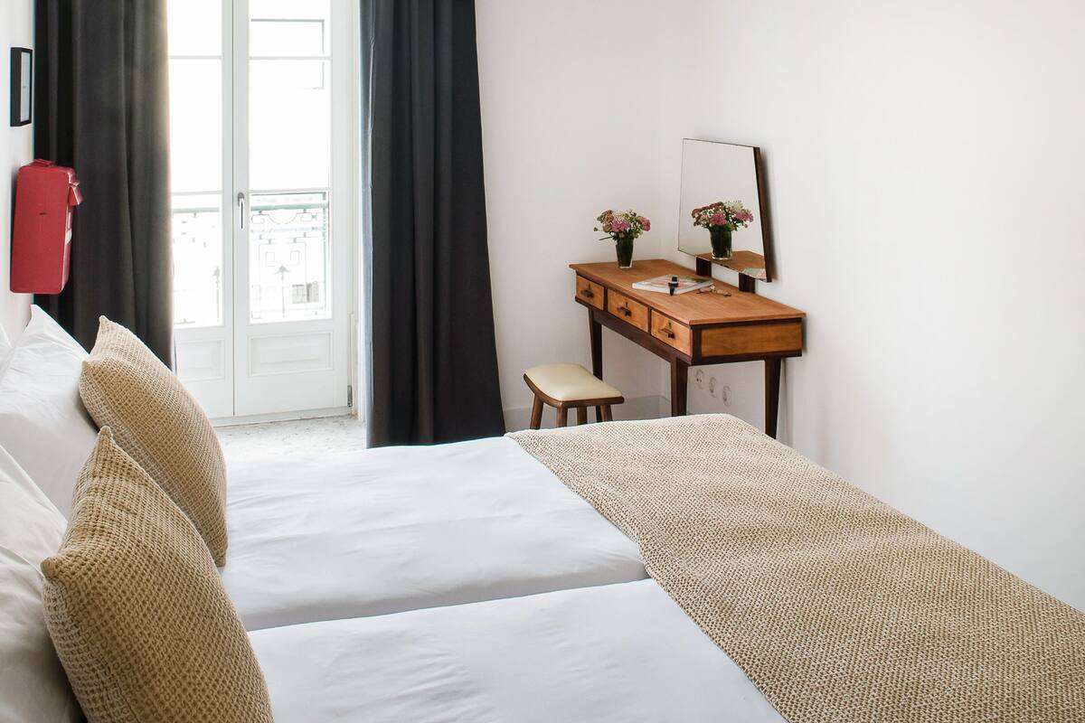 Una habitación de hotel con una cama, un escritorio con espejo y una ventana con cortinas.