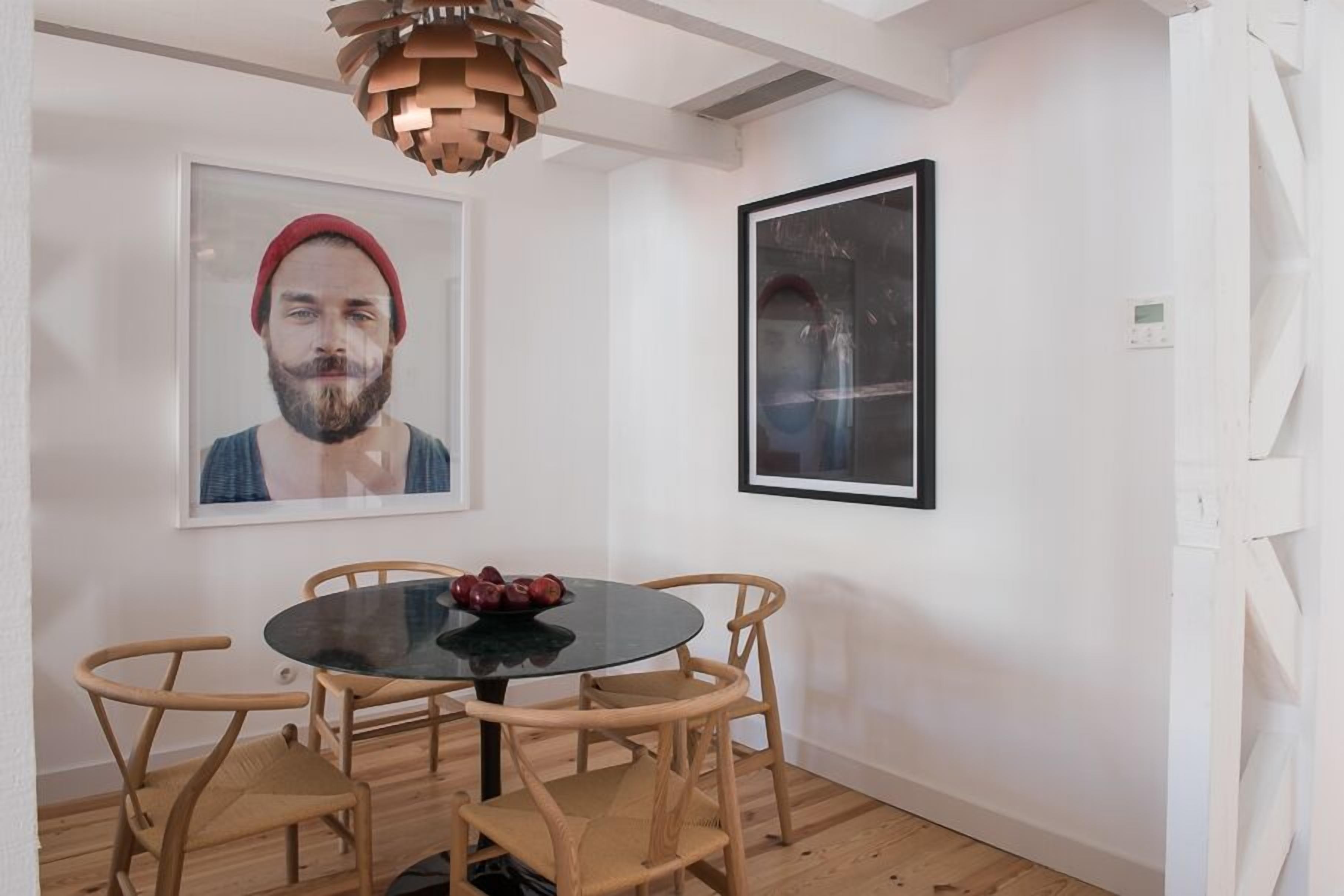 A dining area with a round table, four wooden chairs, a black glass table, and a wooden pendant light.