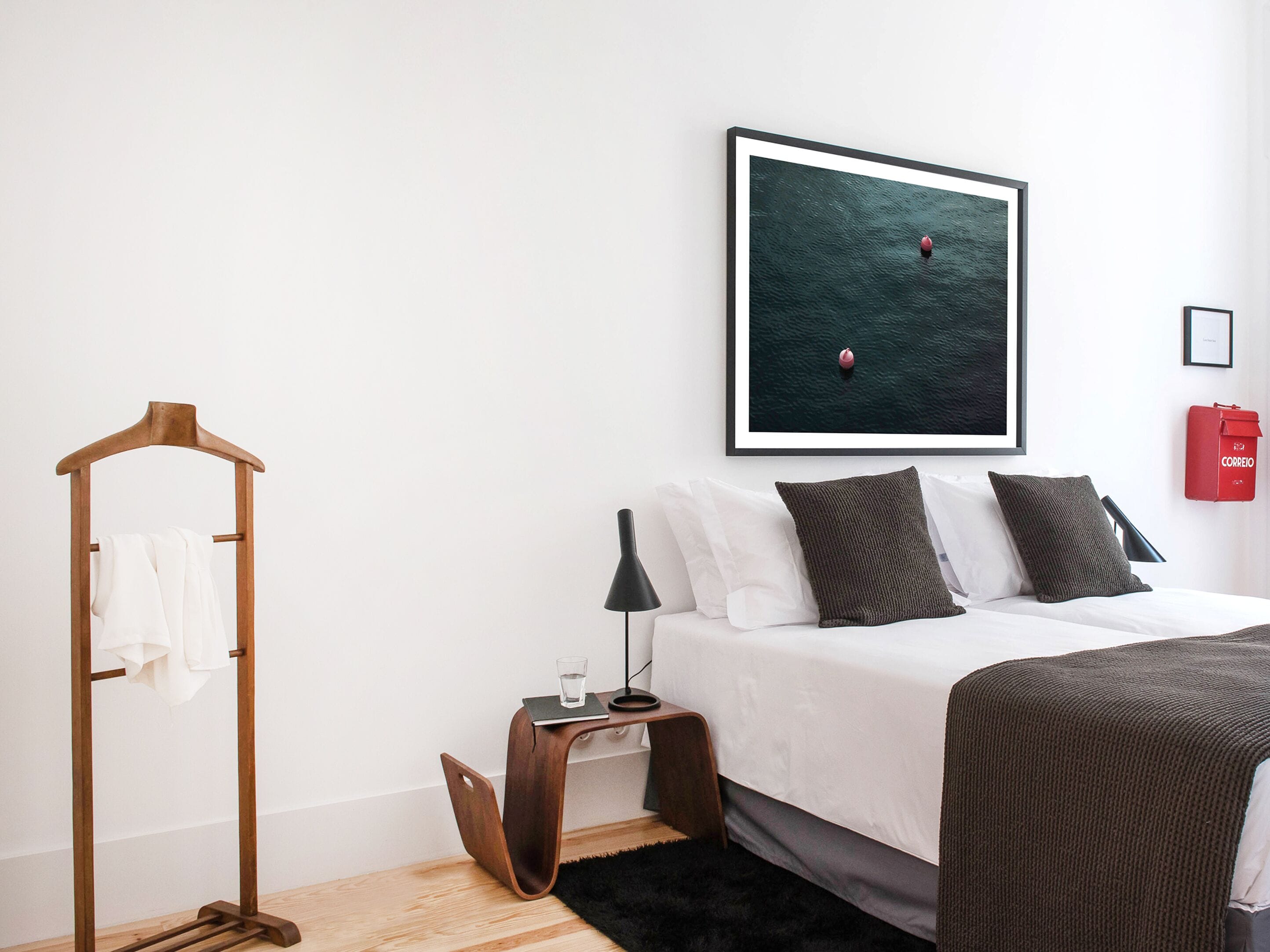 A modern bedroom with a bed, a framed picture of a boat on water, a wooden hanger, and a red mailbox.