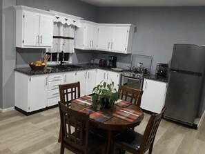 A kitchen with white cabinets, a stainless steel refrigerator, a dining table with chairs, and a coffee maker. - Nature’s bliss/ La Luna  (Choiseul)
