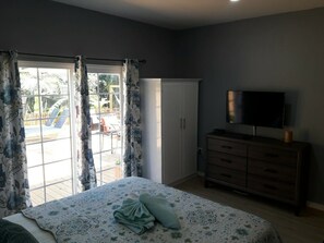 A bedroom with a bed, a TV, a dresser, and a sliding glass door leading to an outdoor area. - Nature’s bliss/ La Luna  (Choiseul)