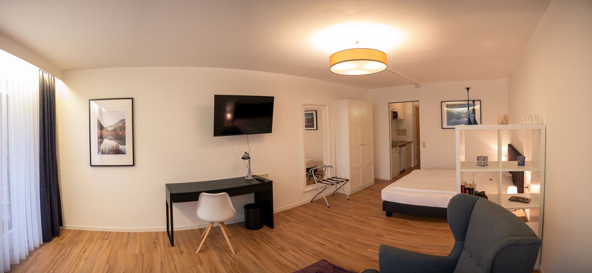 A modern hotel room with a bed, a desk, a chair, a TV, and a wardrobe.