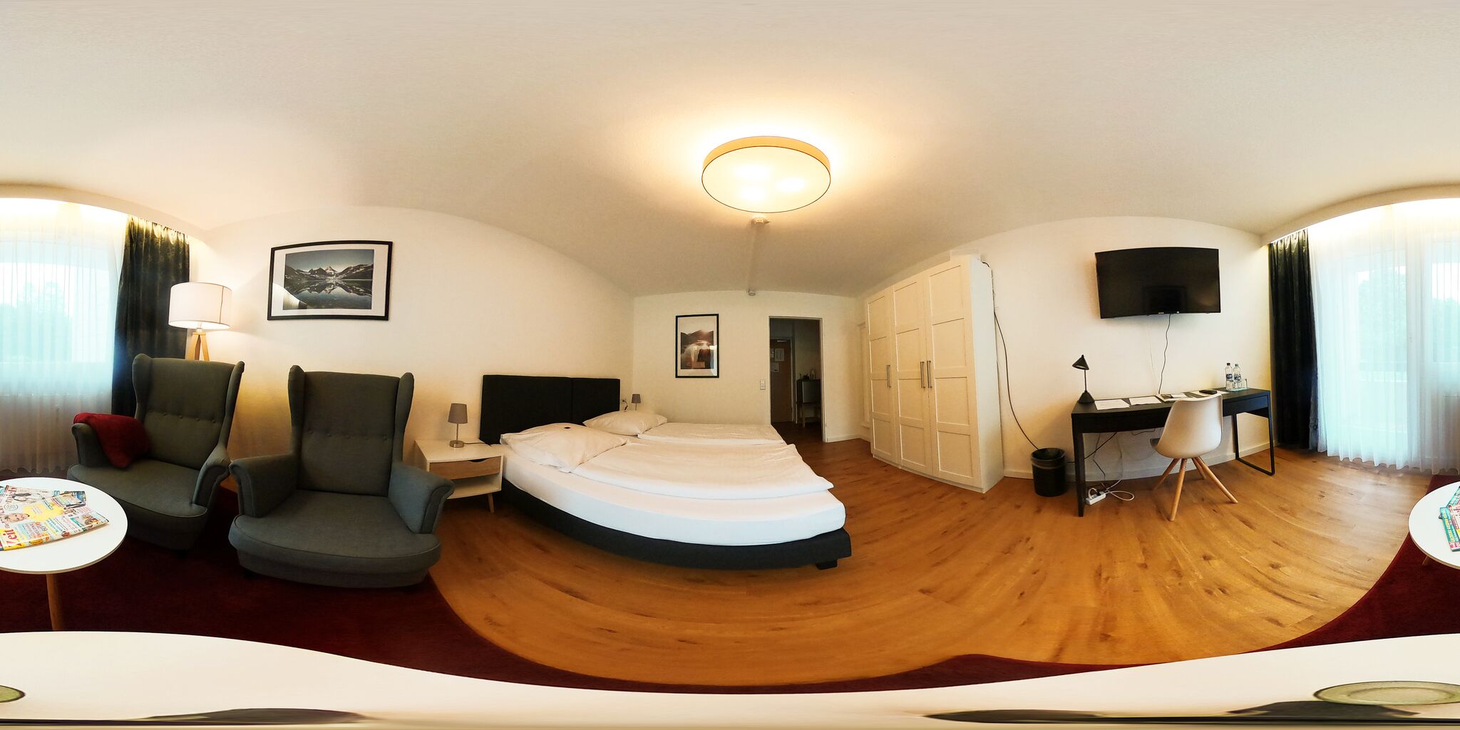 Una habitación con una cama, dos sillones, un escritorio, un televisor y una lámpara en el techo.