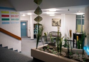 A lobby with a staircase, a reception desk, a bookshelf, and a decorative plant arrangement. - Hotel Quellenhof Bad Urach (Bad Urach)