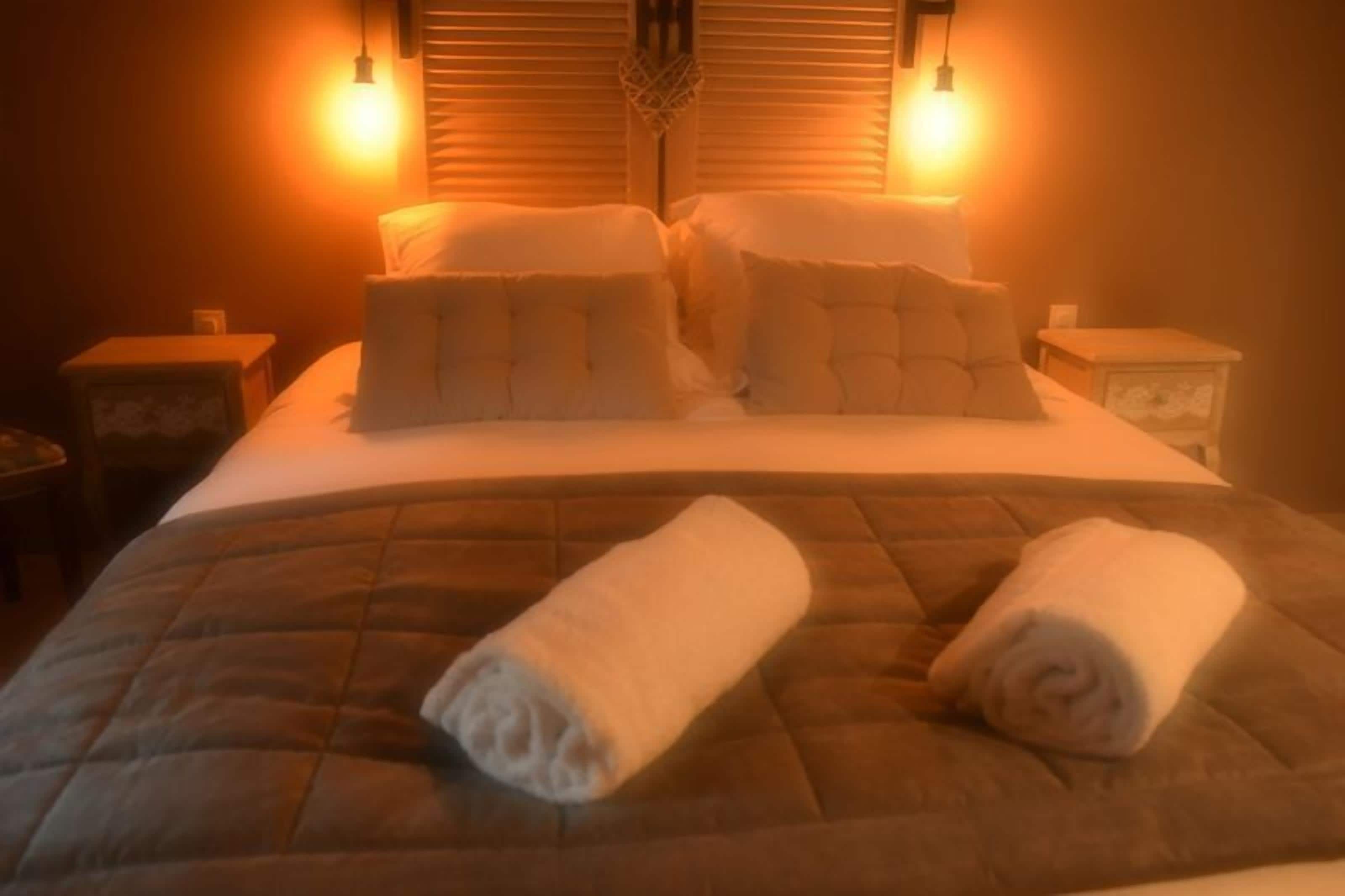 Una cama bien hecha con una colcha acolchada, dos almohadas y dos toallas enrolladas sobre la cama.