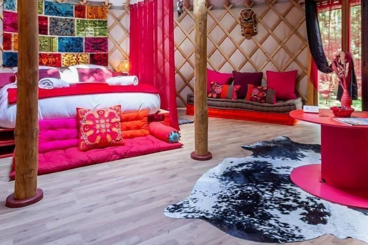 Eine Jurte mit runder Decke, bunten Wandteppichen, einem zentralen Bett mit roter Bettwäsche und einem roten und schwarzen Teppich auf dem Boden.