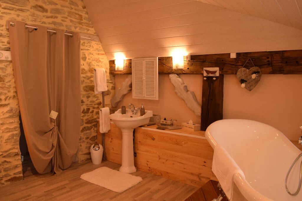 A bathroom with a stone wall, wooden vanity, a white sink, a bathtub, and a towel rack.
