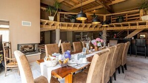 Un espace repas doté d’un plafond en bois, de plusieurs suspensions décoratives et d’une longue table à manger dressée pour le repas.