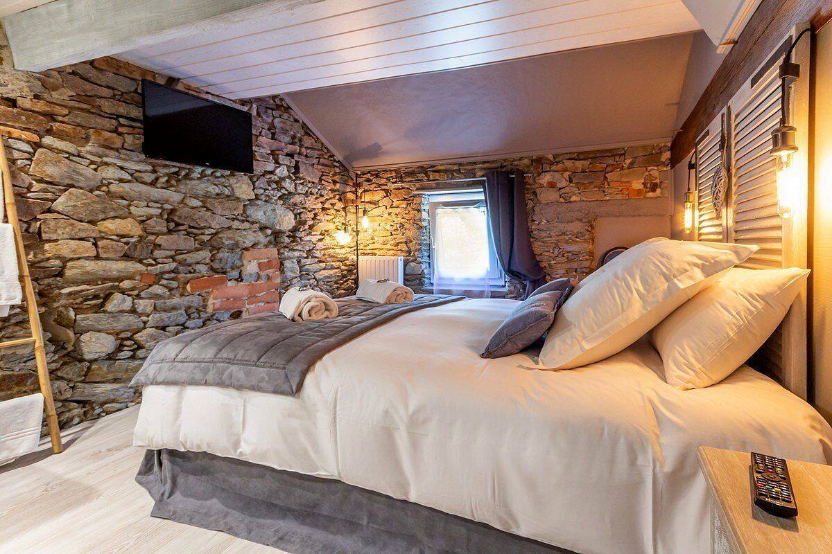 Ein Schlafzimmer mit Steingemäuer, einem Bett mit weißer Bettwäsche, einer Fernbedienung auf einem Nachttisch und einem Fenster mit Vorhängen.