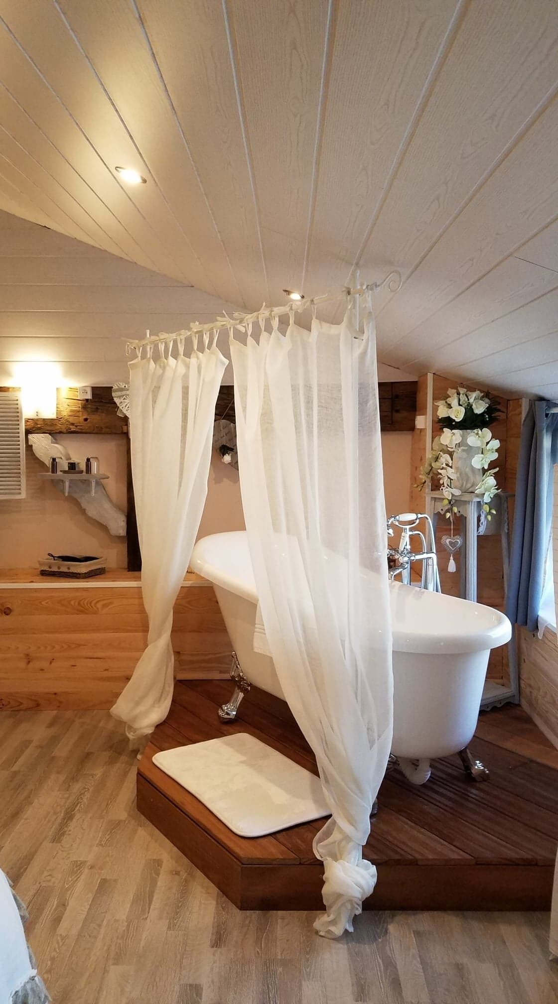 Un baño con una bañera independiente, suelo de madera y techo con vigas a la vista.