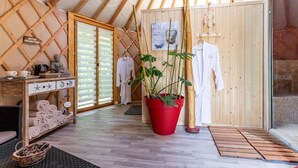Une pièce chaleureuse avec un plafond en bois, une grande plante rouge en pot et des robes blanches accrochées au mur.