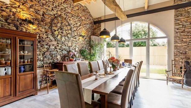 Un espace repas agrémenté d’un mur en pierre, de poutres en bois et d’une grande fenêtre.