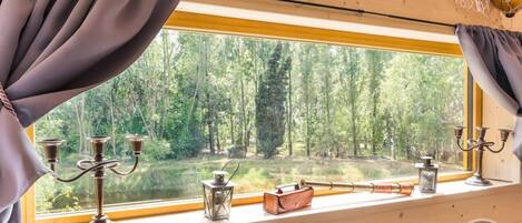 A room with a large window overlooking a forest, wooden walls, and a window sill with decorative items.