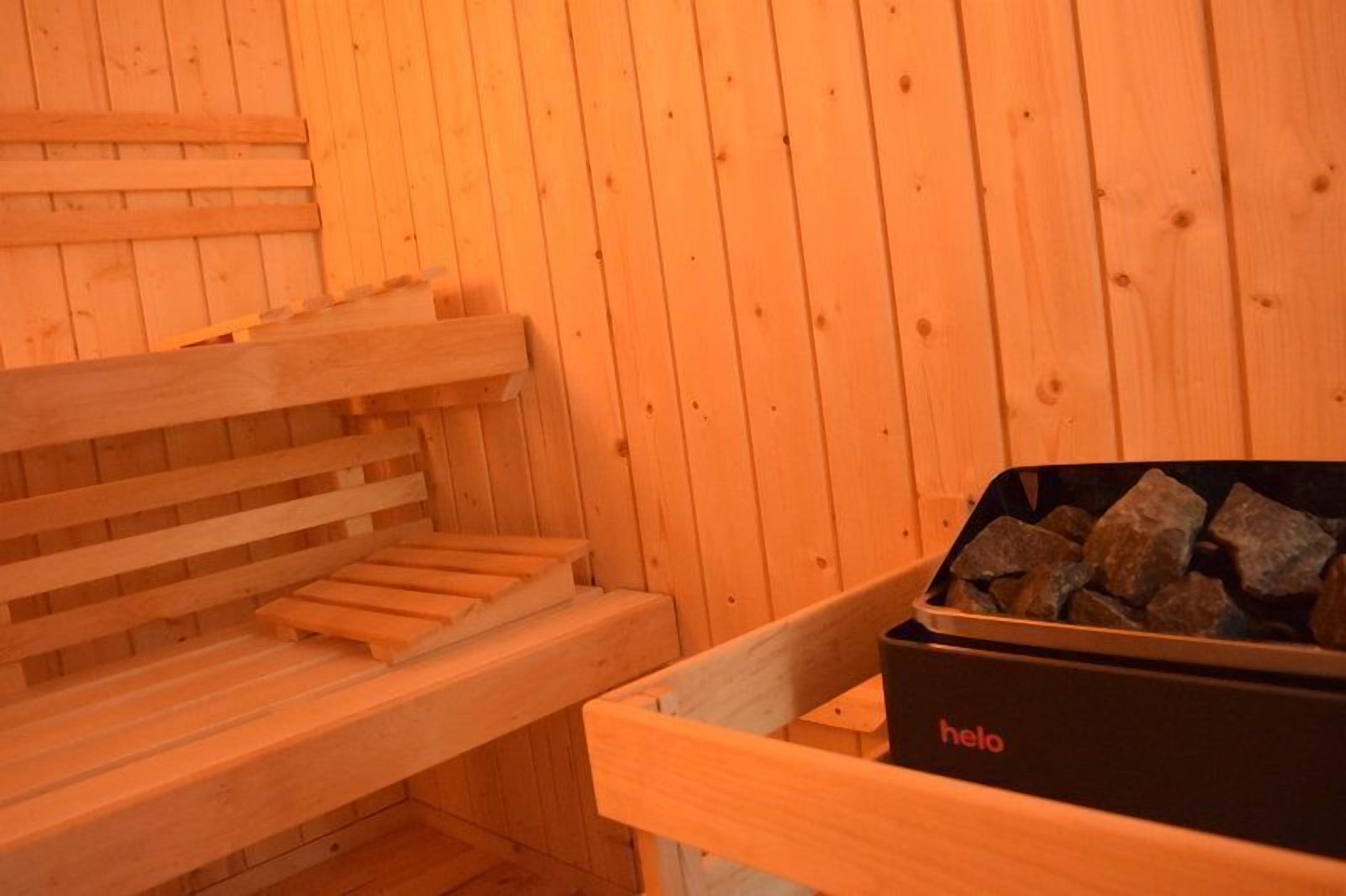 Un sauna avec des bancs en bois et un récipient noir portant l’inscription « helo » et contenant des pierres.