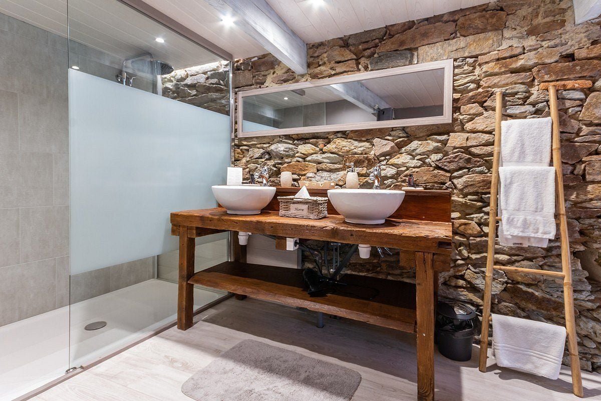 A bathroom with a stone wall, a wooden vanity with two sinks, a mirror, and a towel rack.
