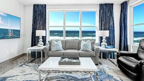 Ein Wohnzimmer mit Meerblick, ein graues Sofa mit gemusterten Kissen, ein schwarzer Ledersessel und ein Couchtisch mit Dekorationselementen.