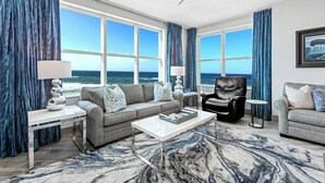 Ein modernes Wohnzimmer mit einem großen Fenster und Blick auf den Ozean, eine Couch, ein Couchtisch und ein Ledersessel.