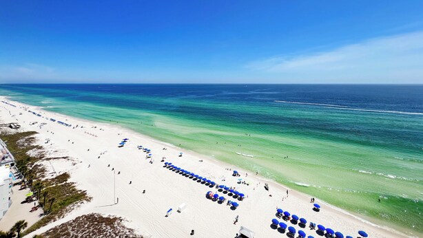 Ein Strand mit Reihen blauer Sonnenschirme und Liegestühle, ein klarer, blauer Himmel und das Meer.