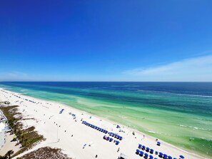 Ein Strand mit Reihen blauer Sonnenschirme und Liegestühle, ein klarer, blauer Himmel und das Meer.