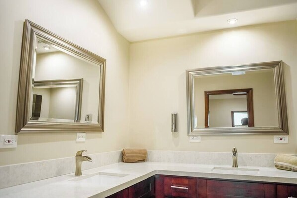 Une salle de bain moderne avec deux vasques, de grands miroirs et un meuble-lavabo avec des armoires en bois foncé.